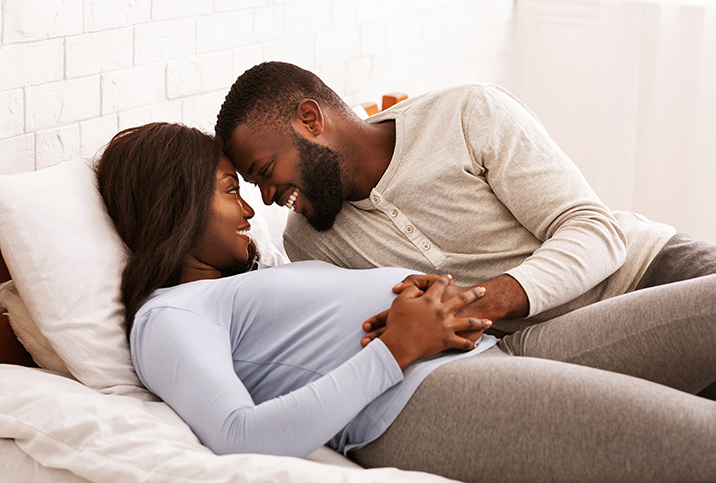 man and pregnant woman cuddle in bed and smile at each other