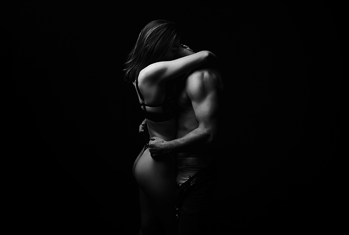A couple stands and embraces each other intimately while under low light.