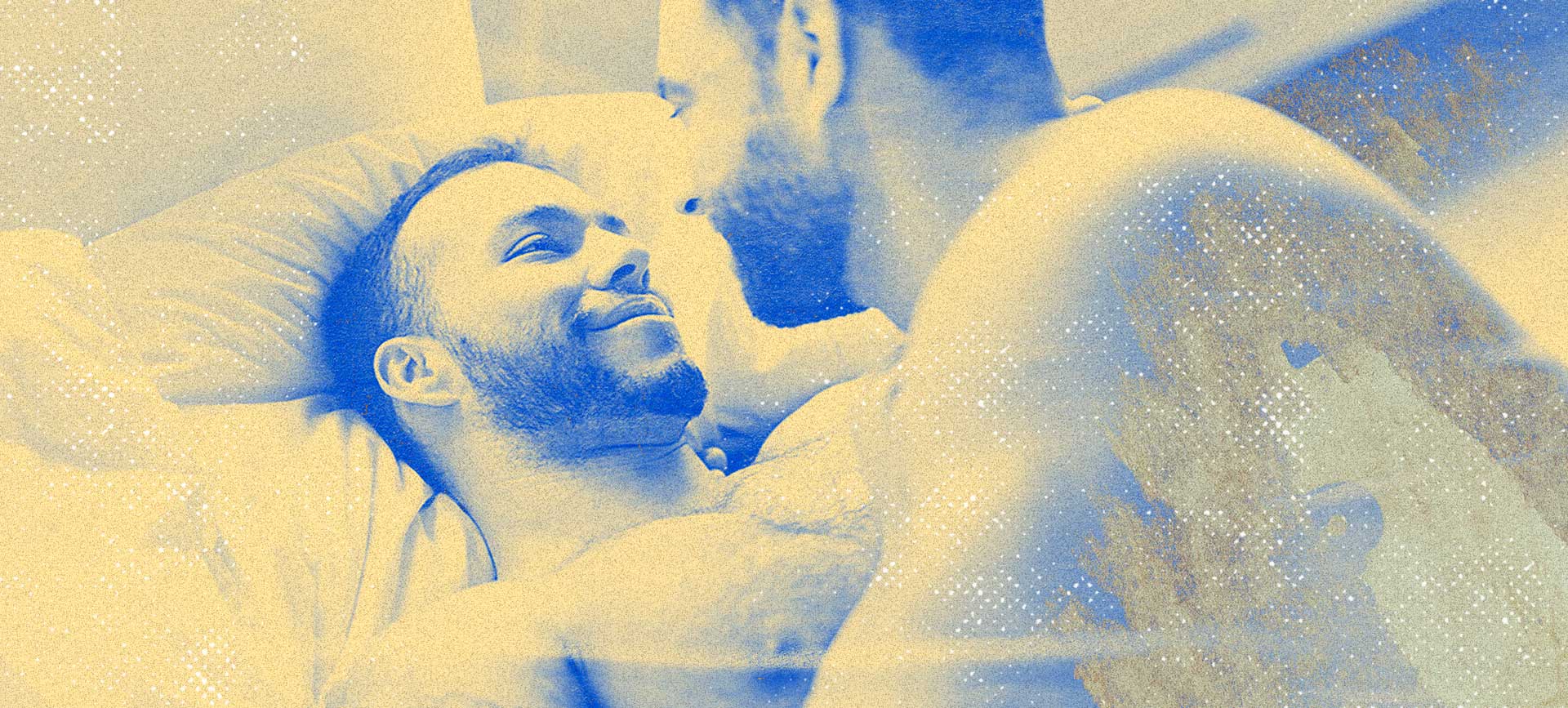 Two men lay in bed smiling at each other.