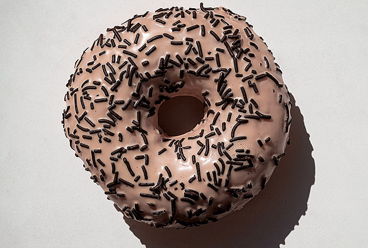 A pink donut with black sprinkles against a white background.