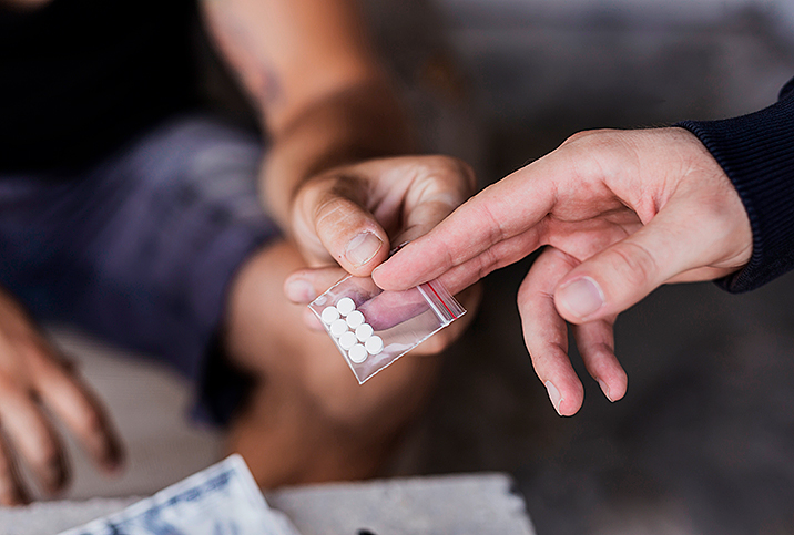 hands pass small baggie of white pills to other hands