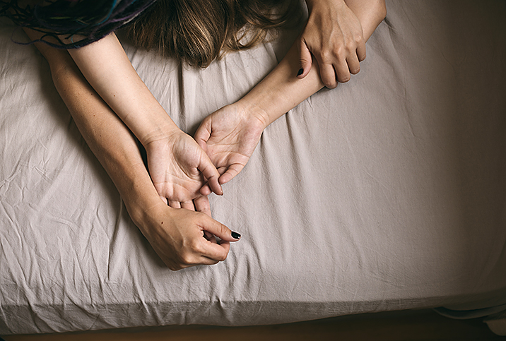 Two people lying together in bed with outstretched arms.