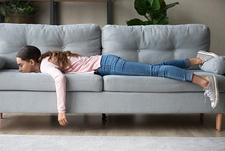 A woman lying on a grey couch tired from her period.