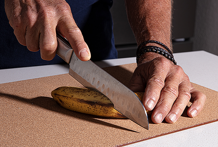 hands with kitchen knife slice into a banana on cutting board