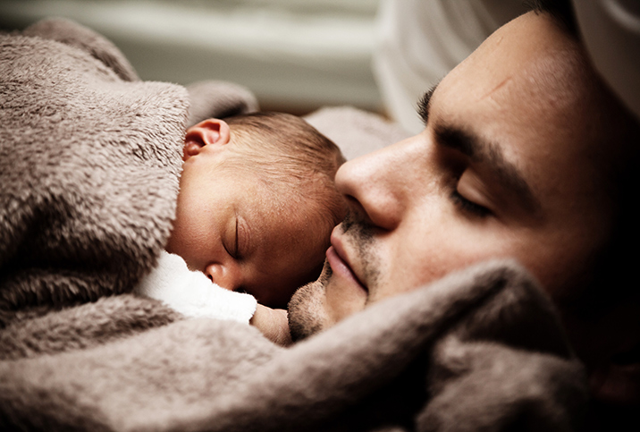 A father holds his newborn baby on his chest while laying down.