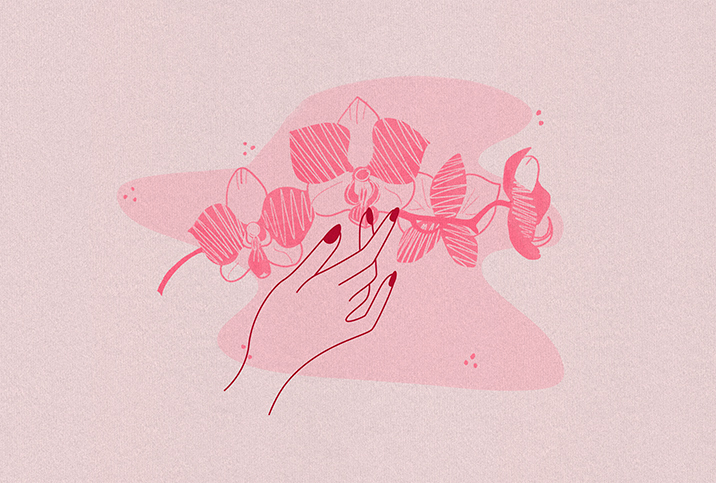 female hand lightly touches pink orchid on pink background