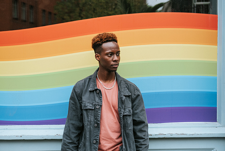 A person standing in front of a rainbow graphic.