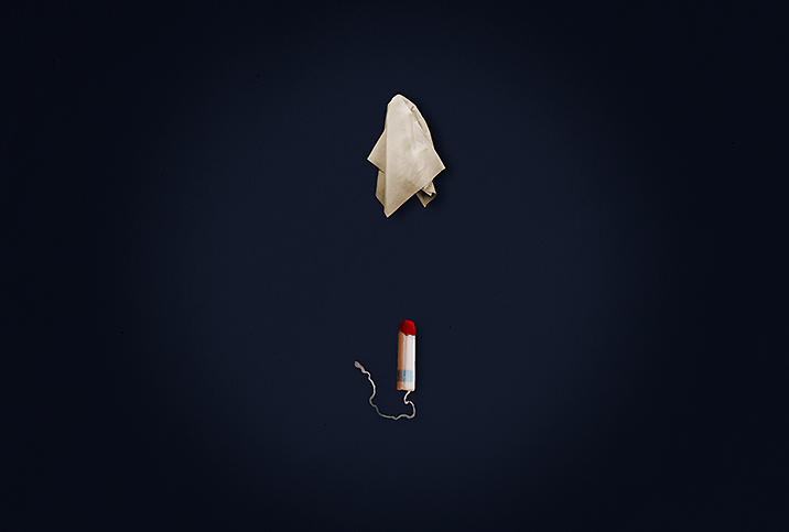 A tissue hovers above a tampon with blood on the tip against a dark blue background.