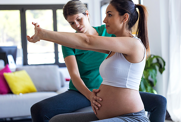 pregnant woman exercises with arms outstretched as other woman touches her belly