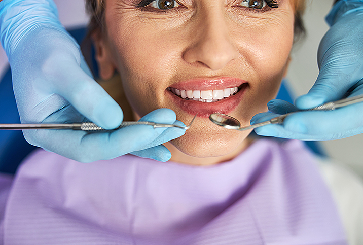 A woman receiving a dental exam from a dentist wearing blue gloves.