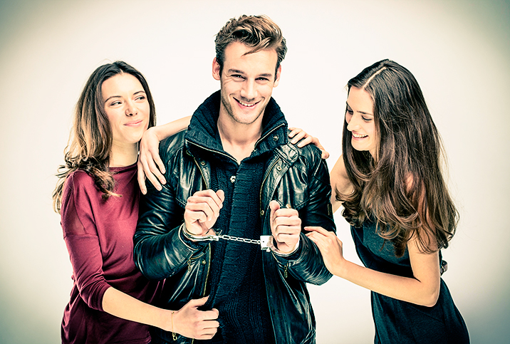 A man is smiling and handcuffed as he stands between two women.