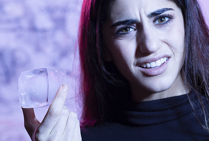 A woman with a confused look holding an ice cube.