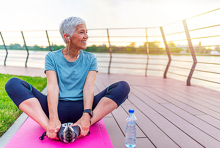 older woman smiles as she stretches doing yoga outside