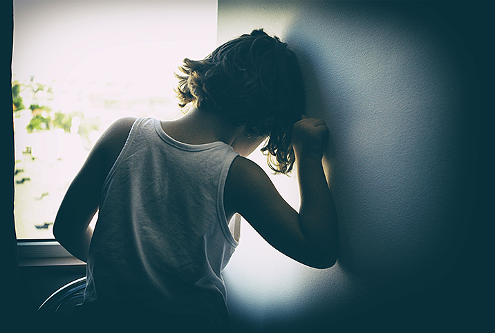 child with short hair and white top leans in wall with head in their hand