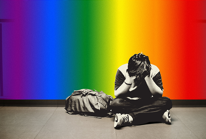 A child sits on the ground with his legs crossed and head in his hands against a rainbow wall.