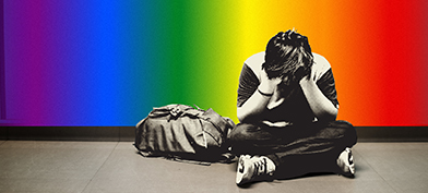 A child sits on the ground with his legs crossed and head in his hands against a rainbow wall.