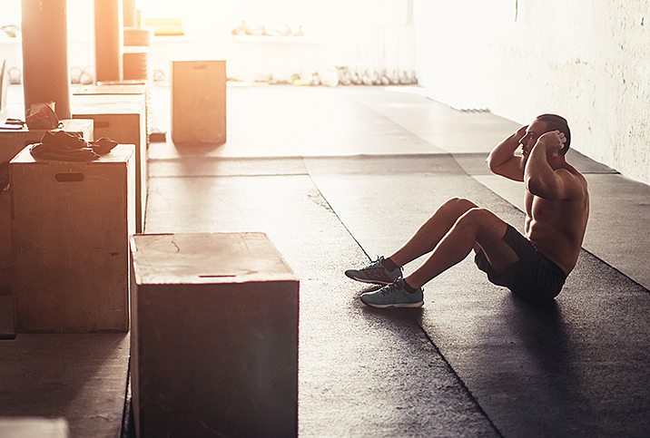 A man is doing sit-ups in the gym with sunlight shining through the window.