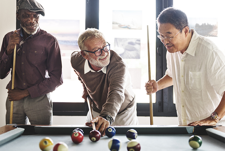 three older men smile at each other as they play pool