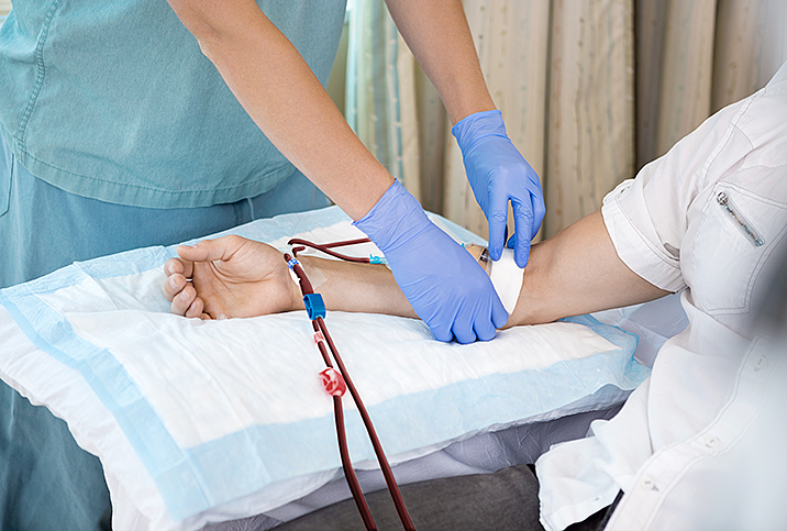 blue gloved hands take blood sample from patient in white shirt