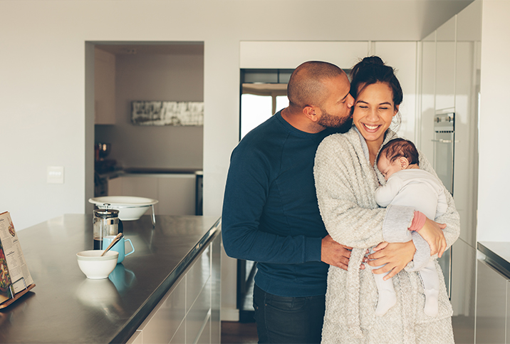 Man-kisses-a-woman-holding-a-baby-in-the-kitchen