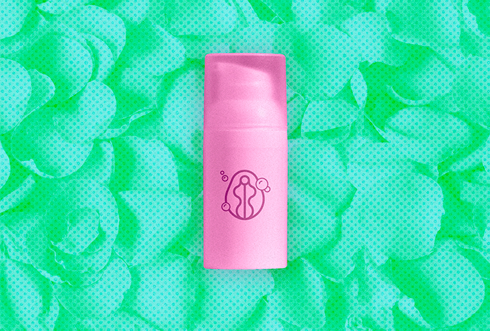 pink-skincare-bottle-sits-against-green-pile-of-petals