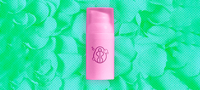 pink-skincare-bottle-sits-against-green-pile-of-petals