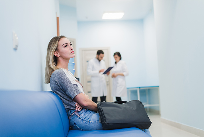 A woman sits on a hospital bench with two doctors in the background.