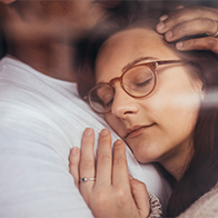 A woman in glasses rest her cheek against her spouse's chest.