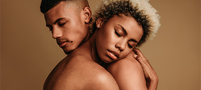 A naked couple embraces with their eyes closed. 