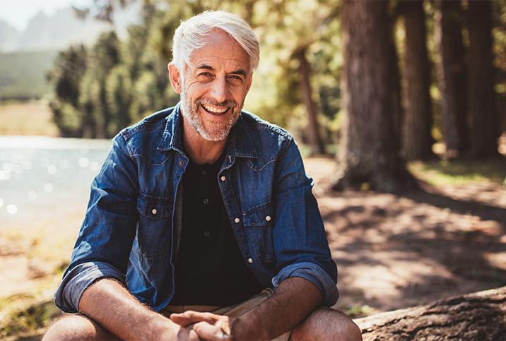 A-white-haired-man-sits-in-the-wood-smiling-at-the-camera