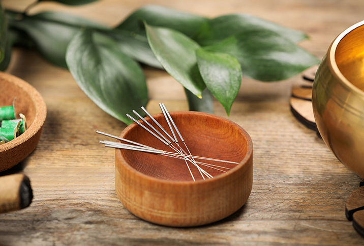 A wooden bowl is holding acupuncture needles.