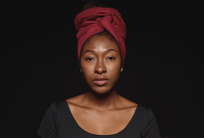 A black woman wearing a head wrap looks at the camera.