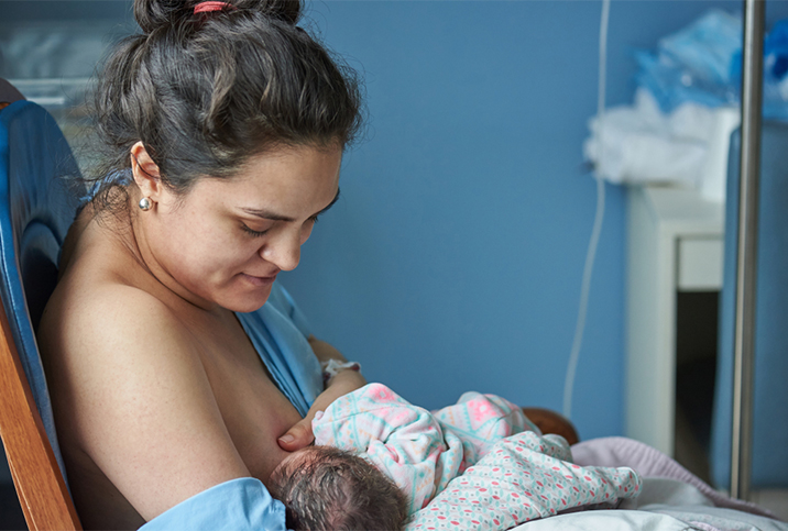 A woman nurses her baby in a blue hospital room. 