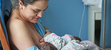 A woman nurses her baby in a blue hospital room. 
