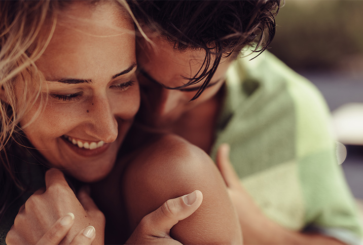 A man nuzzles into a smiling woman's shoulder. 