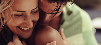 A man nuzzles into a smiling woman's shoulder. 