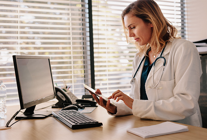 A doctor sits at a desk and looks at a tablet. 