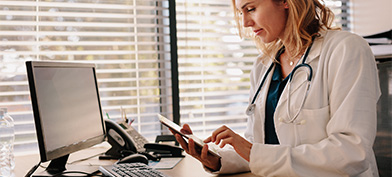 A doctor sits at a desk and looks at a tablet. 