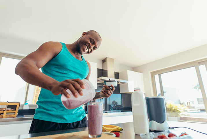 A smiling man pours himself a purple smoothie.