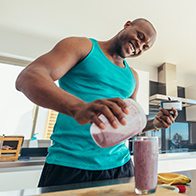 A smiling man pours himself a purple smoothie.