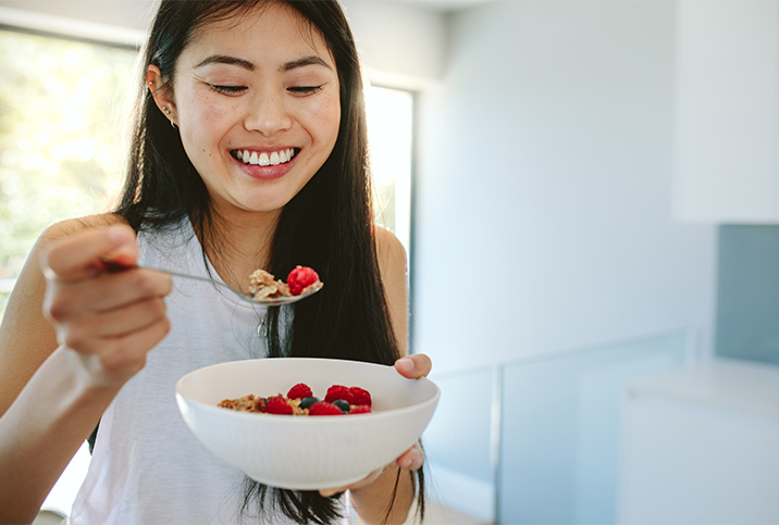 A smiling woman eats granola and berries. 