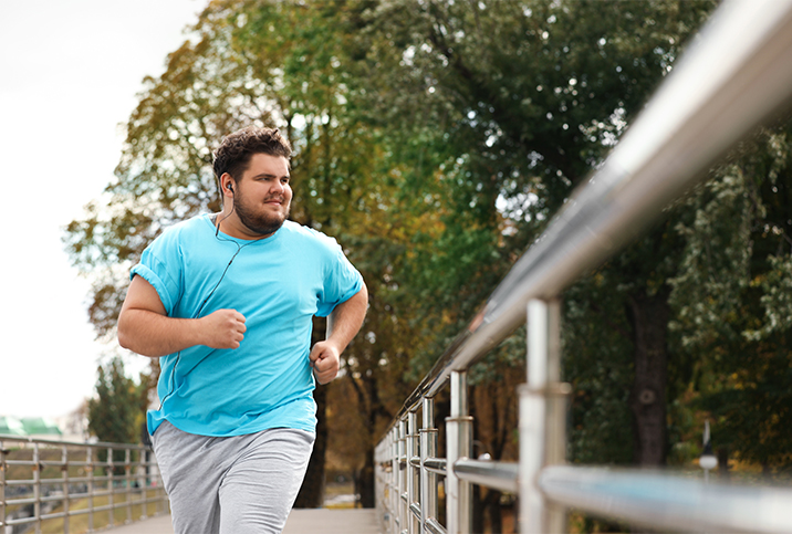 A man runs down the street, wearing blue and listening to music.