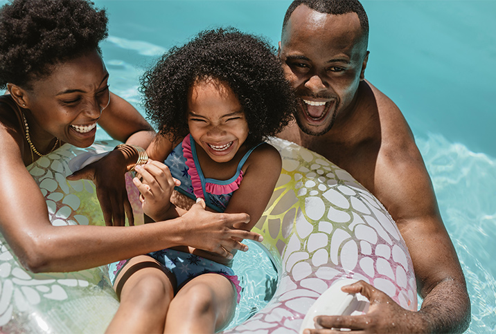 A mother and father laugh as they float in a pool beside their daughter who is in an inner tube.