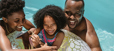 A mother and father laugh as they float in a pool beside their daughter who is in an inner tube.