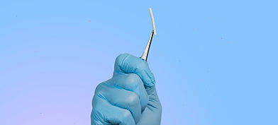 A hand inside of a surgical glove holds a birth control implant between a pair of tweezers.