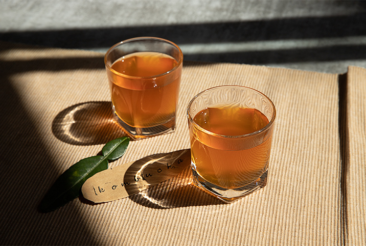 Two glasses of kombucha sit on a table cloth in the sunlight.