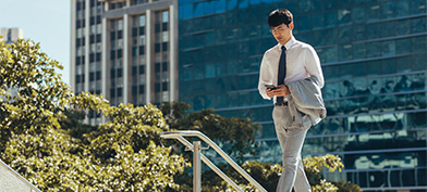 A man in business attire walks in the city while looking at his cellphone.