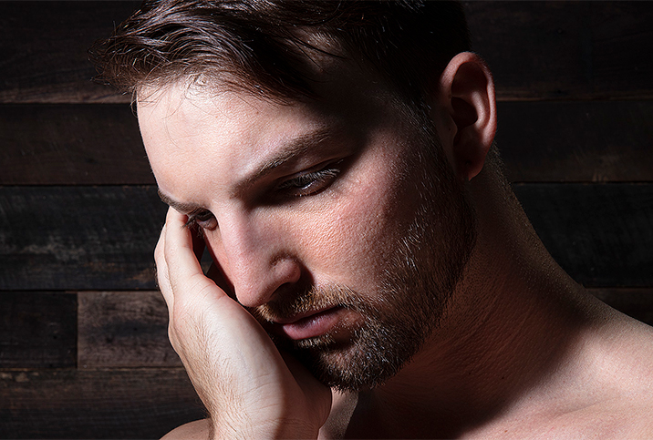 A man rubs his face while looking downward.