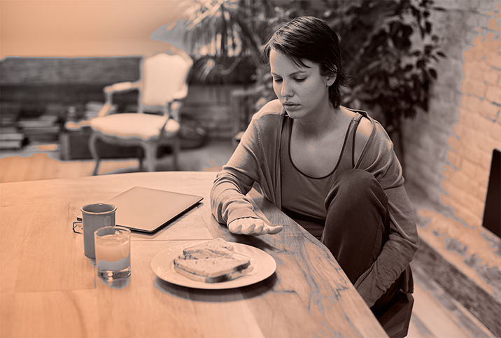 A woman stares tentatively at a plate of food blocked partially by her hand.