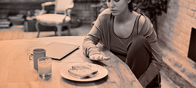 A woman stares tentatively at a plate of food blocked partially by her hand.